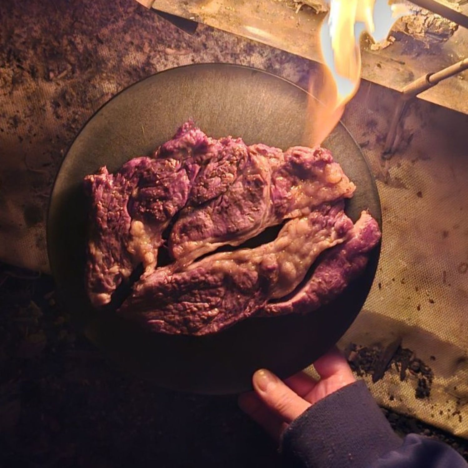 A steak served on a CHOPLATE near a campfire, highlighting its use as a durable camping cutting board plate.