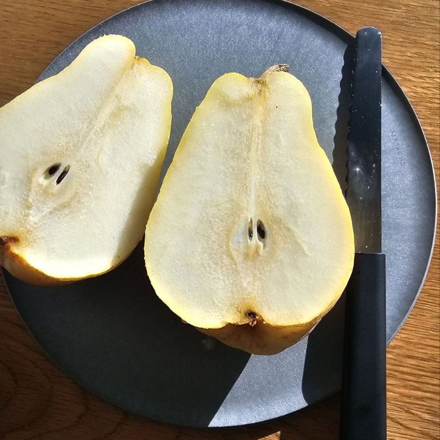 A pear cut in half on a CHOPLATE, demonstrating its functionality as a high-quality Japanese cutting board.
