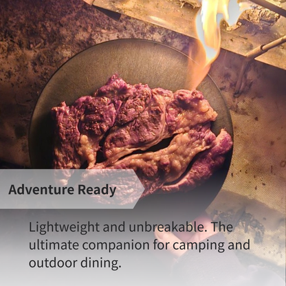 A steak served on a CHOPLATE near a campfire, highlighting its use as a durable camping cutting board plate.